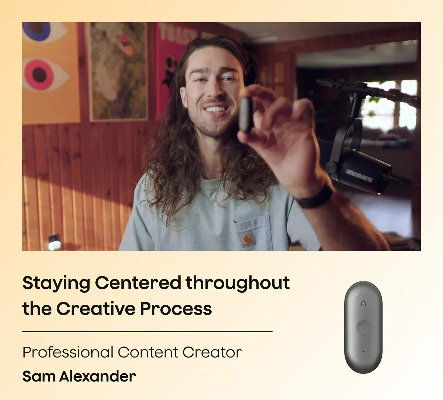 A smiling man with long curly hair holds up a gray Plaud NotePin S in a room with wooden walls and colorful posters.