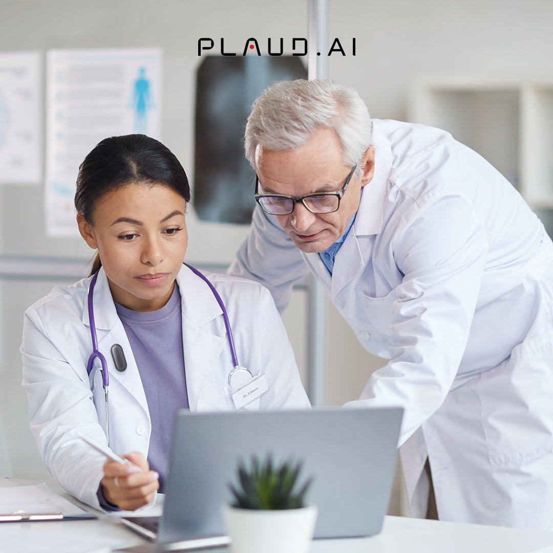 Two doctors in white lab coats intently review a laptop screen, with a black Plaud NotePin S clipped to the woman's lab c