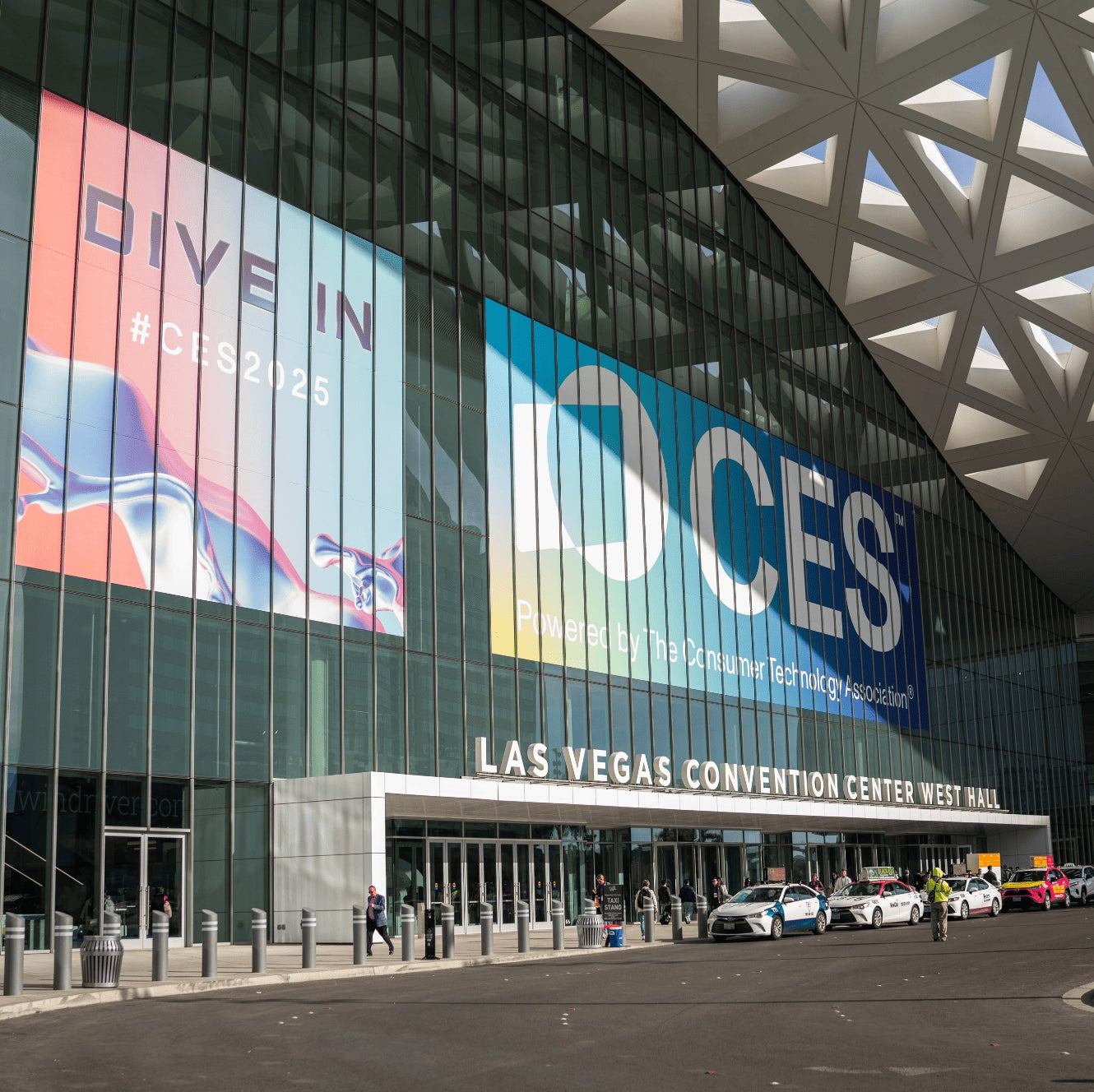 The exterior of the Las Vegas Convention Center West Hall with large CES 2025 banners on its glass facade and cars lined up o