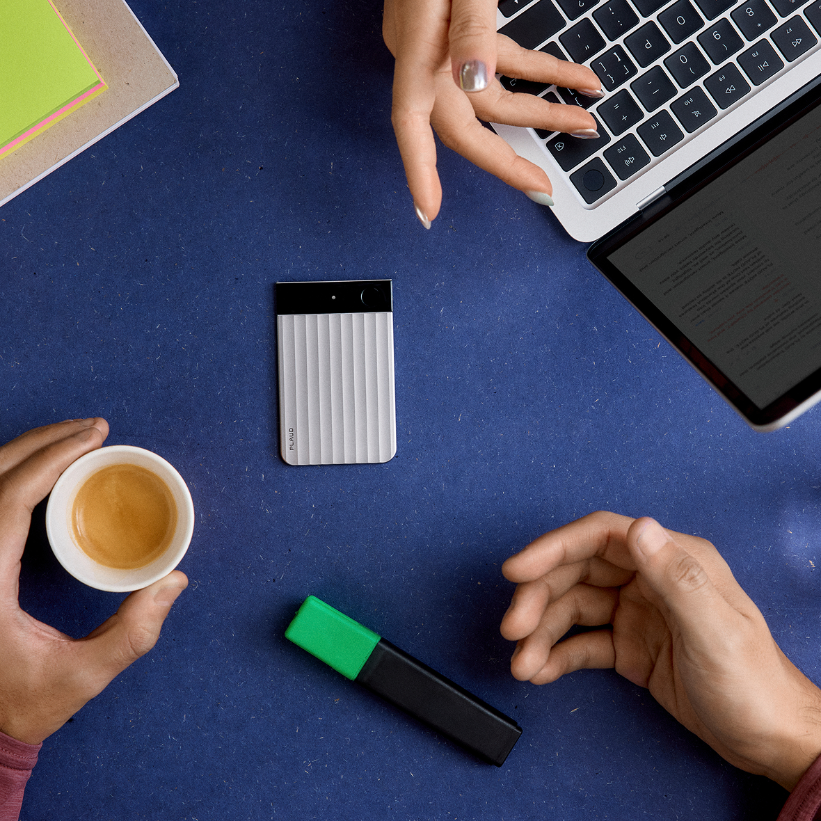Silver Plaud Note Pro on a blue desk with a laptop and coffee.