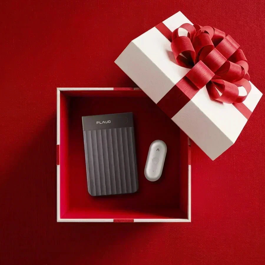 A dark gray Plaud Note and a white Plaud NotePin are nestled inside an open white gift box with a red ribbon on a red backgro