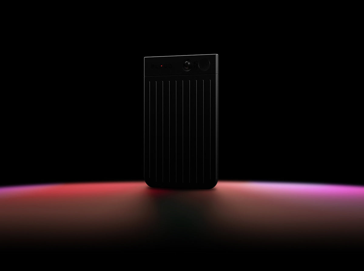 A black Plaud Note stands upright on a dark surface illuminated by a red and purple light gradient.