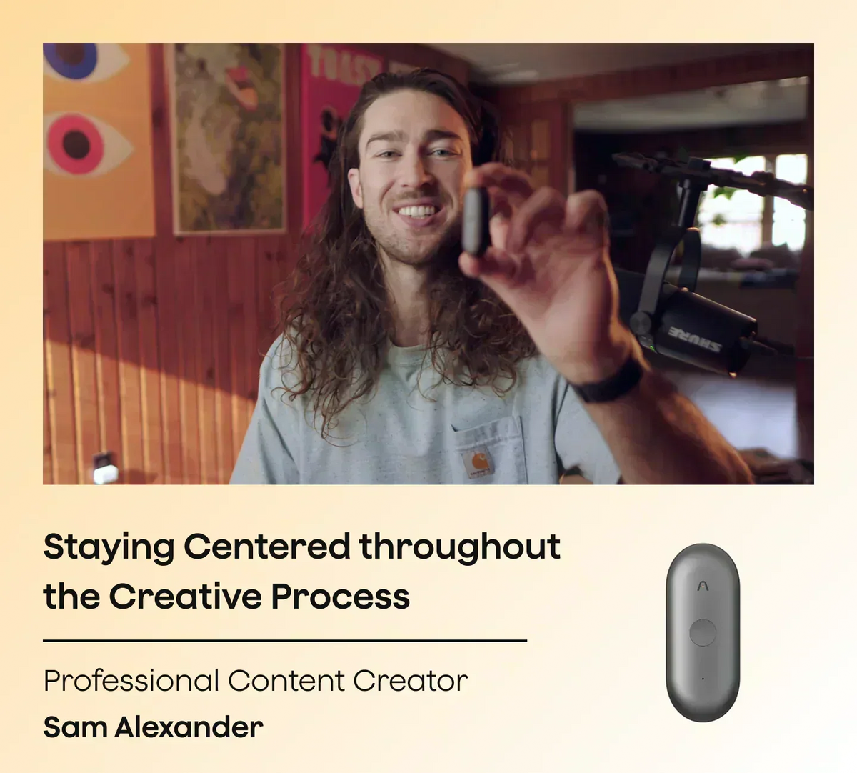 A smiling man with long curly hair holds up a gray Plaud NotePin S in a room with wooden walls and colorful posters.