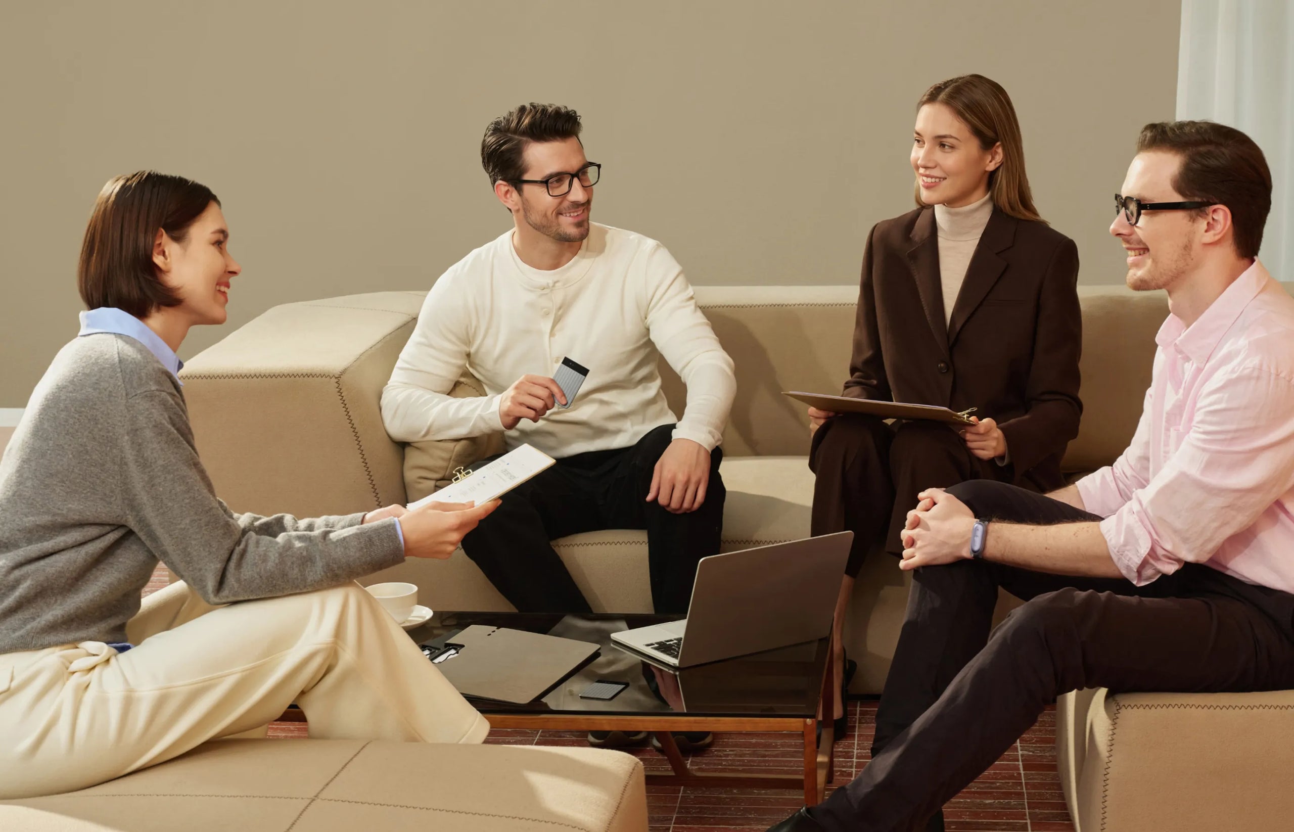 Four smiling people in a casual meeting, with one man holding a black Plaud Note Pro while conversing.