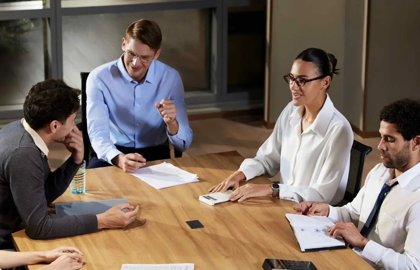 Four professionals discuss around a wooden table, with two Plaud Note Pro AI voice recorders visible on the surface.