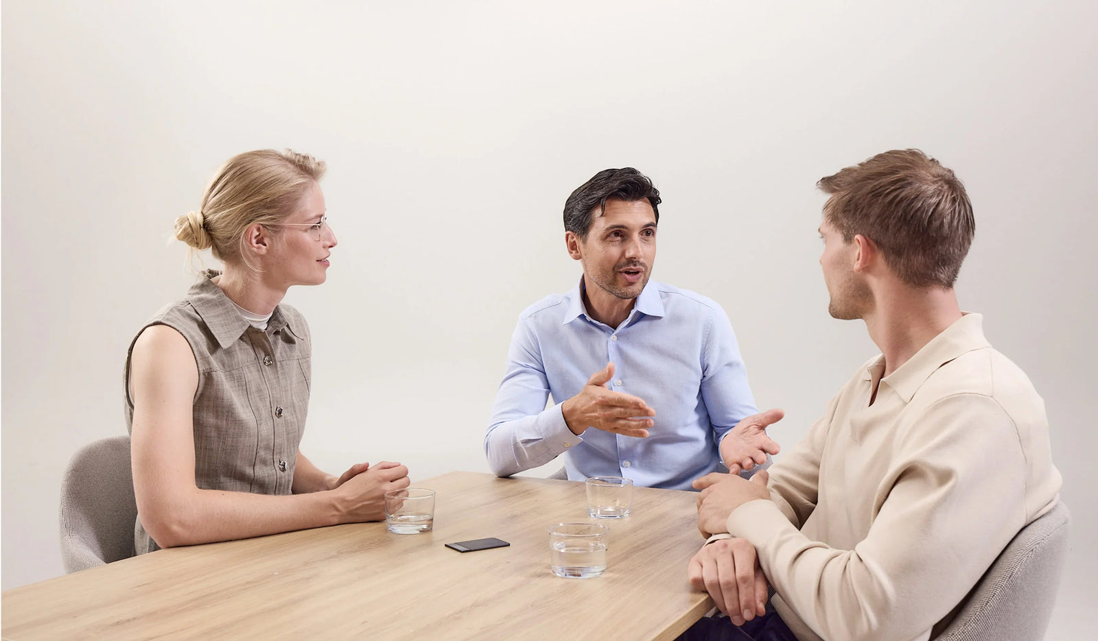 Three professionals engage in a lively discussion around a wooden table, with a black Plaud AI voice recorder capturing their